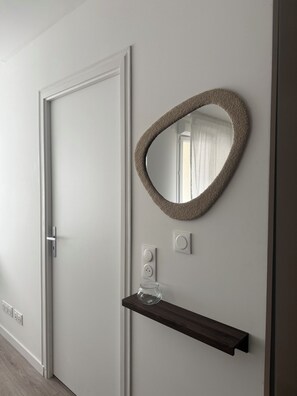 A modern interior with a white door, a wall-mounted mirror, and a wooden shelf with a glass object. - Le Cocon Persan (Persan)