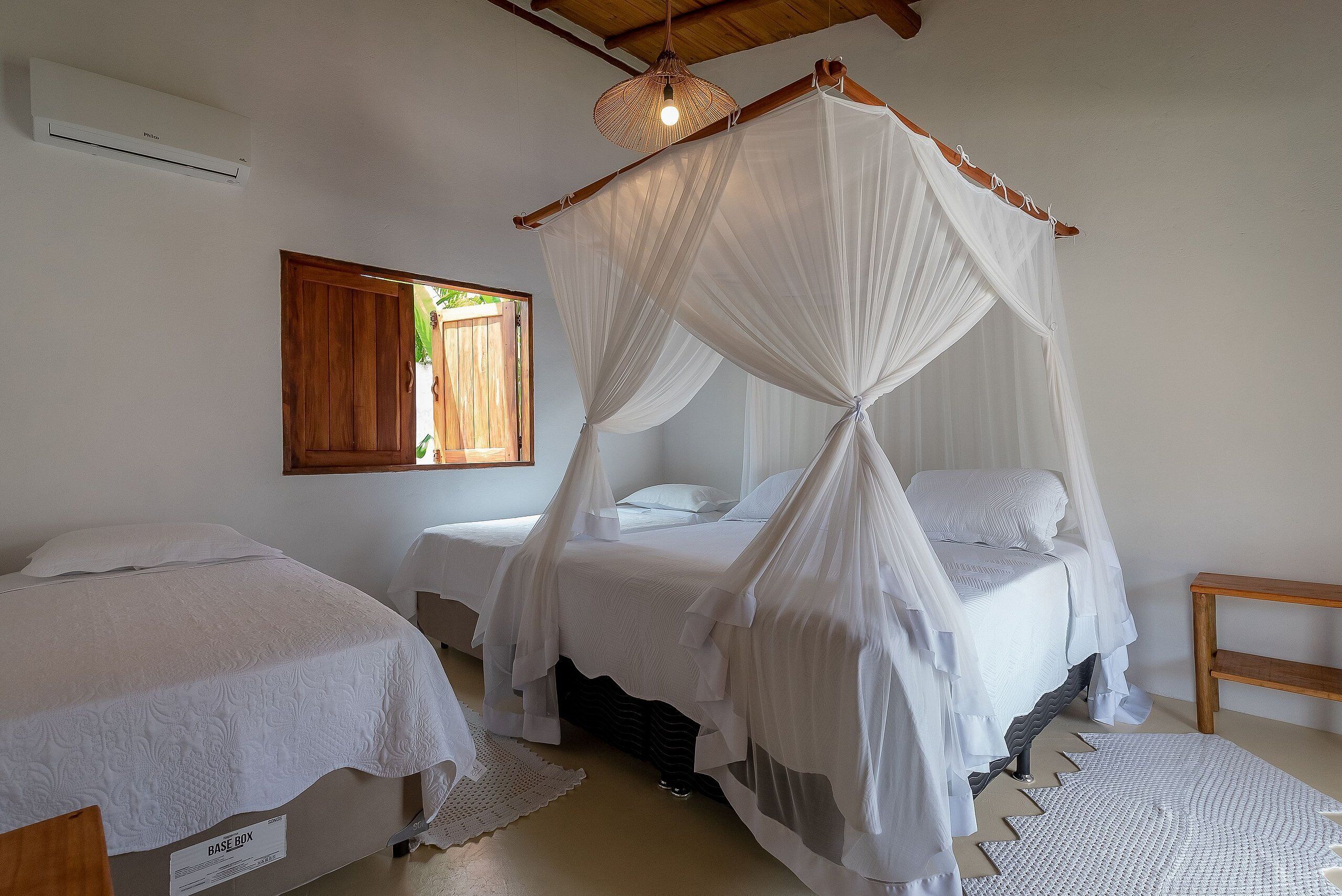 A bedroom with a canopy bed, a bedside table, a base box, and a wooden bench.