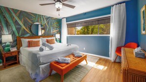 A bedroom with a bed, a bench, a chair, a ceiling fan, a window with curtains, and a wall with a tropical mural. - Paradise Awaits at This Beautiful Waikoloa Village Condo! (Waikoloa Village)