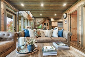 A cozy living room with a brown leather sofa, a coffee table with books and a candle, and wooden walls. - FreeDollywoodTix•Views•Pool•Luxury•Modern•HotTub (Gatlinburg)