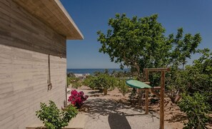 Ein Holzbau mit Blick auf das Meer, eine hölzerne Bank und ein grüner Tisch.