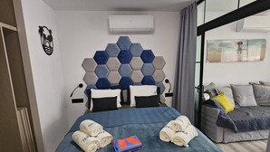 A hotel room with a bed, a headboard with hexagonal tiles, a window with a view, and a ceiling light. - Modern Premium Apartment Near Ccyumbo (San Bartolomé de Tirajana)