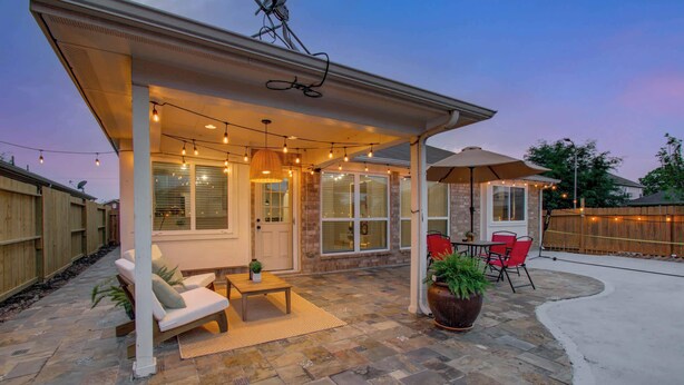 A covered patio with outdoor seating, string lights, and a large umbrella. - 2 Homes • 8BR (sleeps 18) • Game Room & Backyards (Houston)