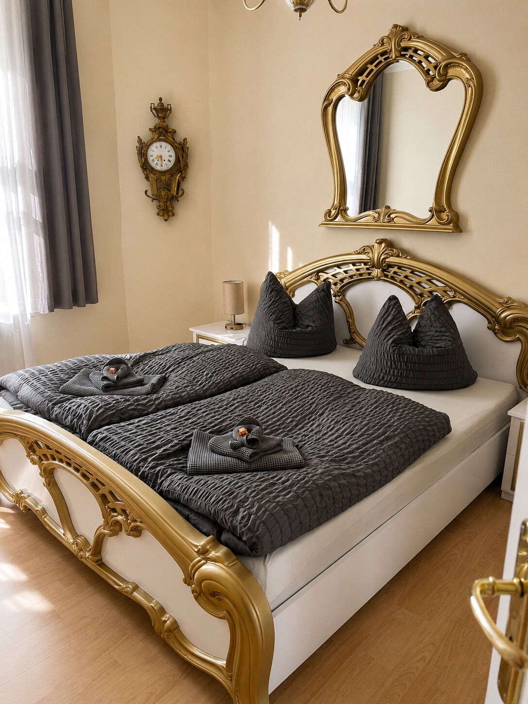 A bed with a gold frame, dark bedding, and a bedside table with a lamp.