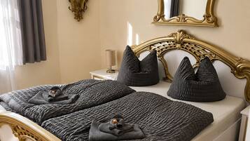 A bed with a gold frame, dark bedding, and a bedside table with a lamp.