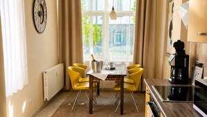 A kitchen with a dining table, yellow chairs, a clock, and a view through the window.