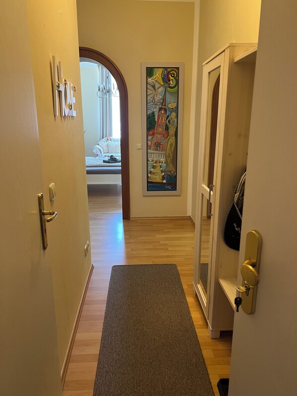 A hallway with a wooden floor, a mat at the entrance, a door with a handle, and a poster on the wall.