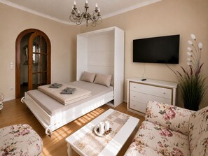 A bedroom with a bed, a TV, a bedside table, a chair, and a large window. - Quiet vacation apartment for 4 guests, 60m² in Bad Elster near forest, pond. Parking lot (Bad Elster)