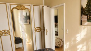 A bedroom with a large bed, a chandelier, a wardrobe with gold accents, and a mirror.
