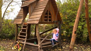 A wooden playhouse with a ladder, a swing, and a bicycle. - Ruhige Ferienwohnung Lachmöwe im Ostseebad Dranske auf Rügen (Dranske)