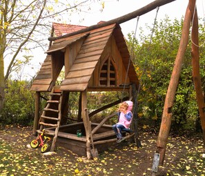 A wooden playhouse with a ladder, a swing, and a bicycle. - Ruhige Ferienwohnung Lachmöwe im Ostseebad Dranske auf Rügen (Dranske)