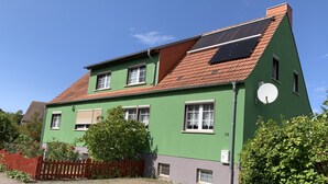A two-story house with a green facade, red roof tiles, and solar panels. - Ruhige Ferienwohnung Lachmöwe im Ostseebad Dranske auf Rügen (Dranske)