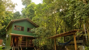 A green house with a wooden deck, surrounded by dense forest. - Chal 3 com Churrasqueira e Ar a 200m da Praia (Prado)