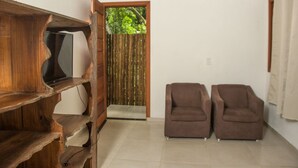 A room with a wooden TV stand, two brown sofas, a wooden door leading to a balcony, and a tiled floor. - Chal 3 com Churrasqueira e Ar a 200m da Praia (Prado)