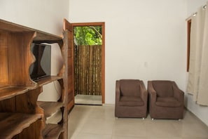 Ein Zimmer mit einem HolztV-Schrank, zwei braunen Sofas, einer Holztür, die auf einen Balkon führt, und einem Fliesenboden.