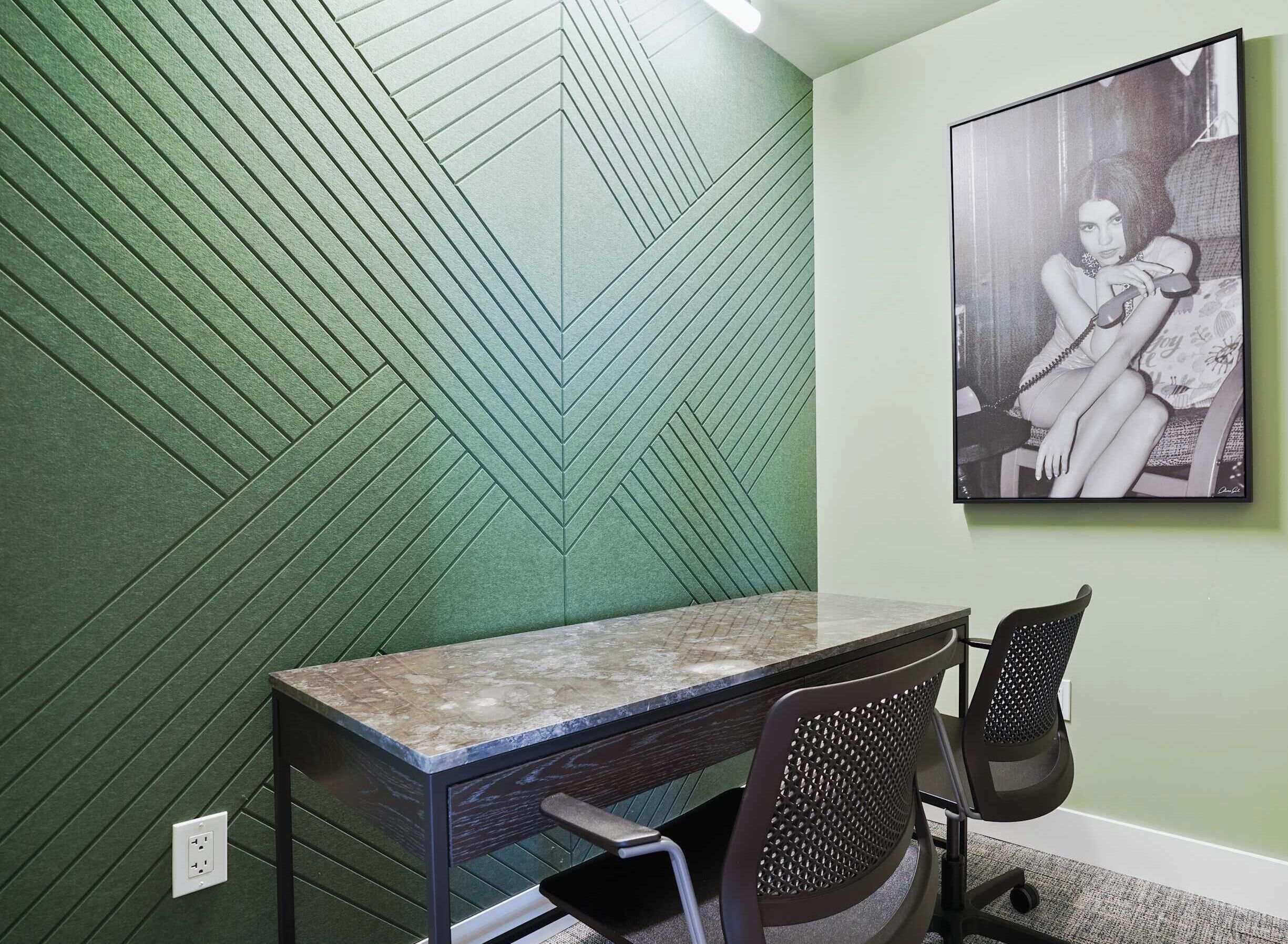 Une pièce avec un mur à la texture verte, un bureau surmonté d’un plateau en marbre, deux chaises de bureau et une photographie en noir et blanc encadrée accrochée au mur.
