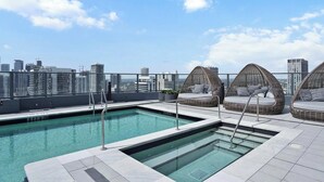 Une piscine sur le toit offrant une vue dégagée sur les gratte-ciel de la ville, dont un bâtiment portant l’inscription « À LOUER 305 ».