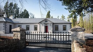 A stone building with a red door, a gravel driveway, and a black metal fence. - Tranquil 7-bedroom villa in charming Dundrum perfect for groups and families. (Dundrum)