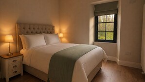A bedroom with a large bed, bedside lamps, a nightstand, a window with a view, and a green throw blanket. - Tranquil 7-bedroom villa in charming Dundrum perfect for groups and families. (Dundrum)