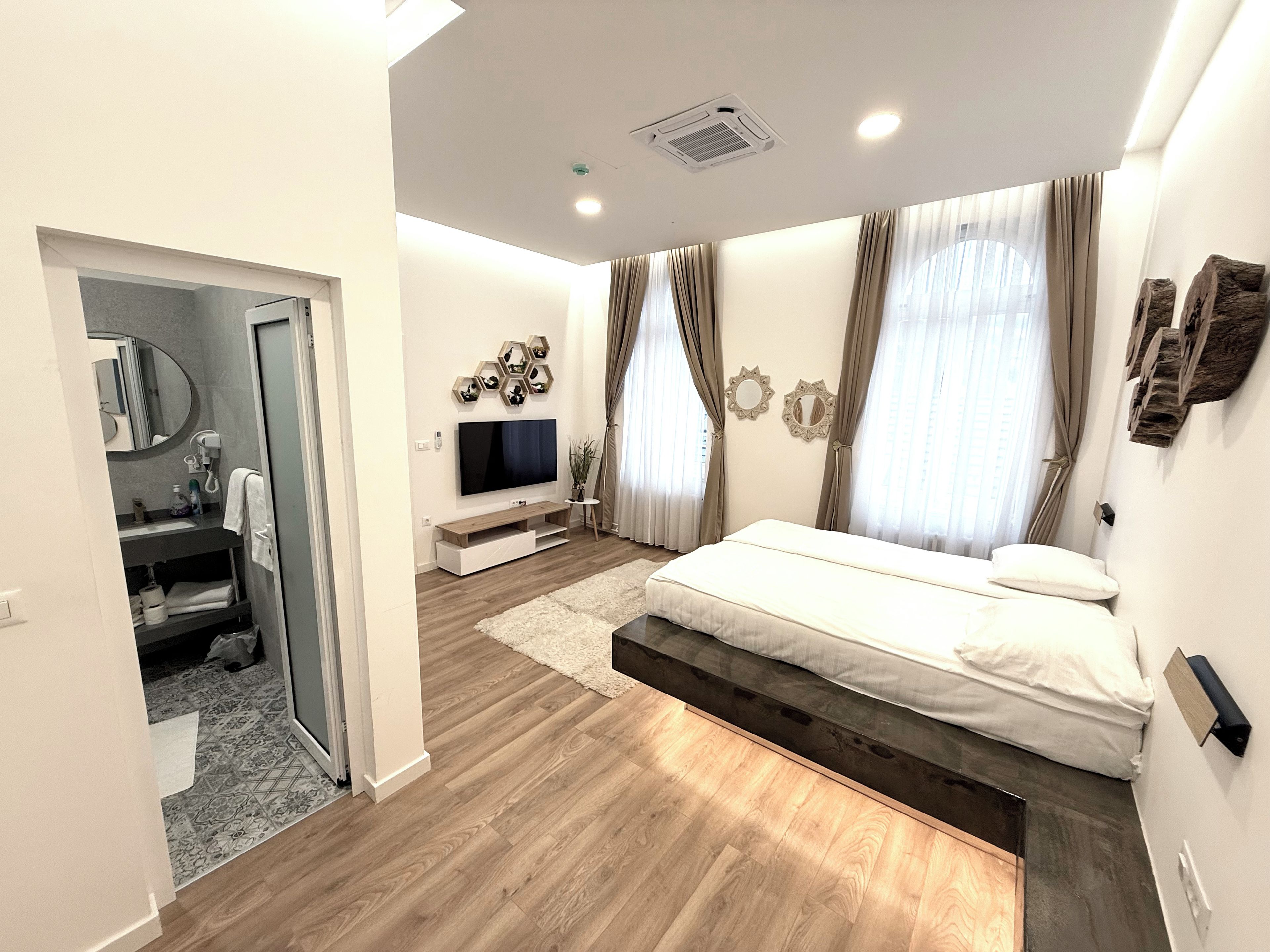A modern bedroom with a bed, a TV, a bathroom, and a living area.
