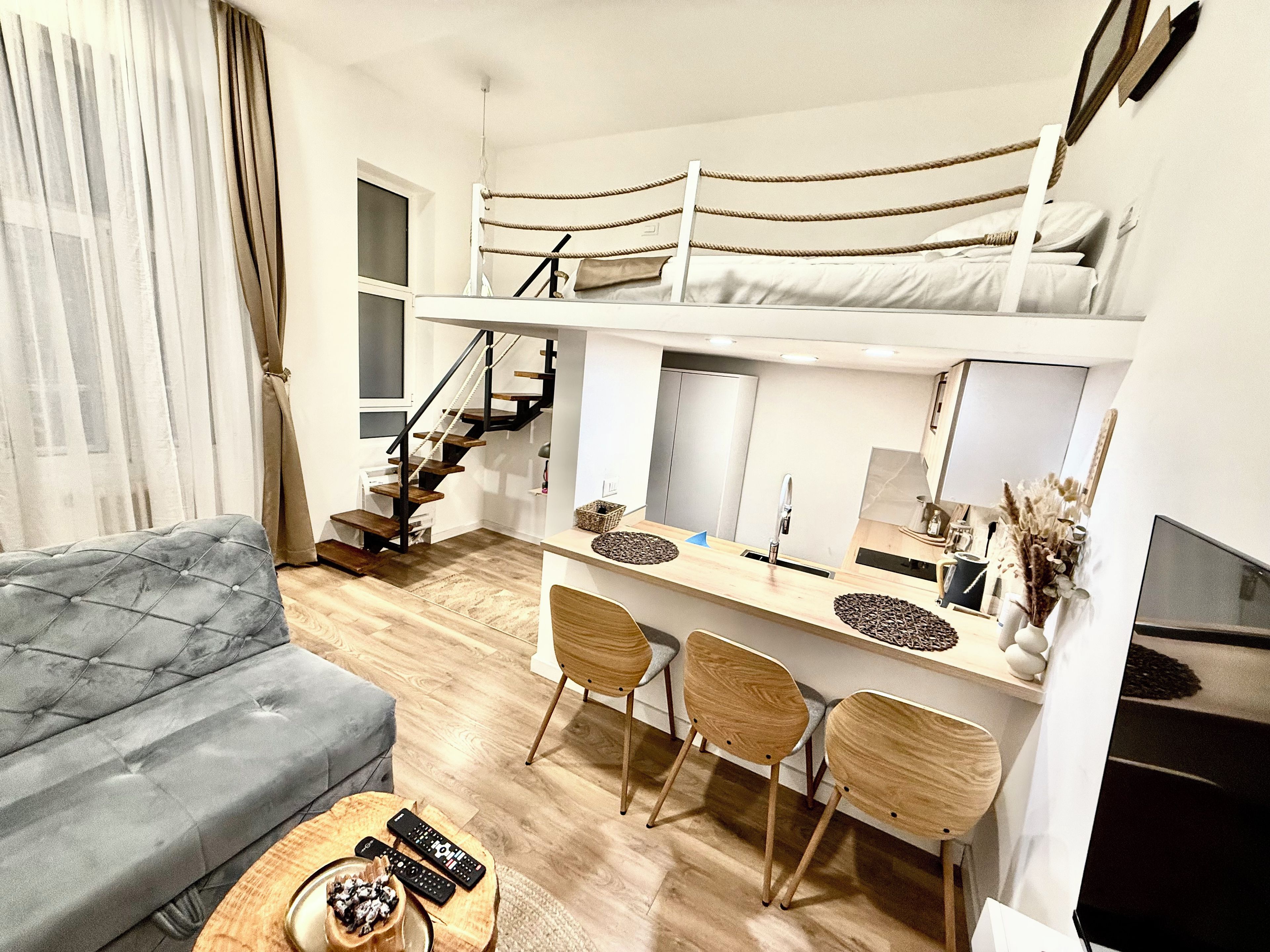Un espacio habitable compacto con una litera, un sofá, una zona de comedor con sillas y un televisor.
