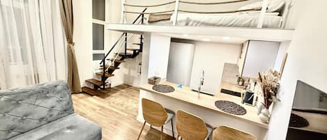Un espacio habitable compacto con una litera, un sofá, una zona de comedor con sillas y un televisor.