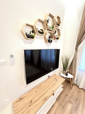 A modern living room with a large flat-screen TV mounted on the wall, wooden hexagonal shelves with decorative items, a wooden coffee table, and a potted plant. - Biospere Lux  (Sarajevo)