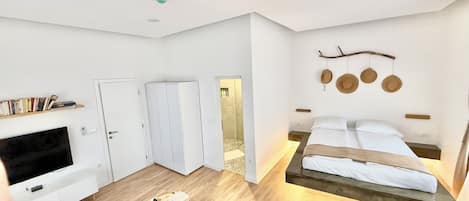 A modern bedroom with a bed, bedside tables, a TV, and a bookshelf.