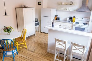 A kitchen with white cabinets, a refrigerator, a stove, and a dining area with a round table and chairs. - Perfect suite for Quebec City visit - wth easy parking (Québec)