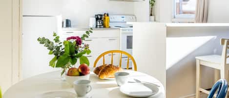 Un comedor con una mesa redonda, sillas, un florero con flores y un croissant.