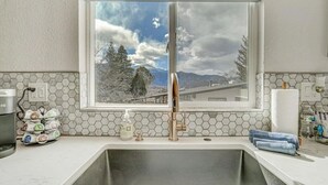 A kitchen with a large window, a stainless steel sink, and a soap dispenser. - PeakView Lil Lux! Hot Tub & Mountain Views (Colorado Springs)