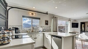 A modern kitchen with a large island, a view of mountains, and a dining area with a view. - PeakView Lil Lux! Hot Tub & Mountain Views (Colorado Springs)