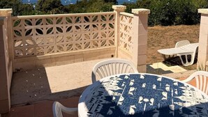 Eine Terrasse mit rundem Tisch und Stühlen, einem Zierzaun und Blick auf das Meer und die Berge.