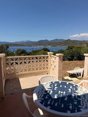 A patio with a round table and chairs, a decorative fence, and a view of the sea and mountains. - Beautiful one-bedroom apartment in a house with a view of the sea, a 5-minute walk from the beach. (Calcatoggio)