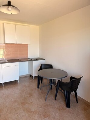 A compact kitchen with white cabinets, a black countertop, and a round table with two chairs. - Beautiful one-bedroom apartment in a house with a view of the sea, a 5-minute walk from the beach. (Calcatoggio)