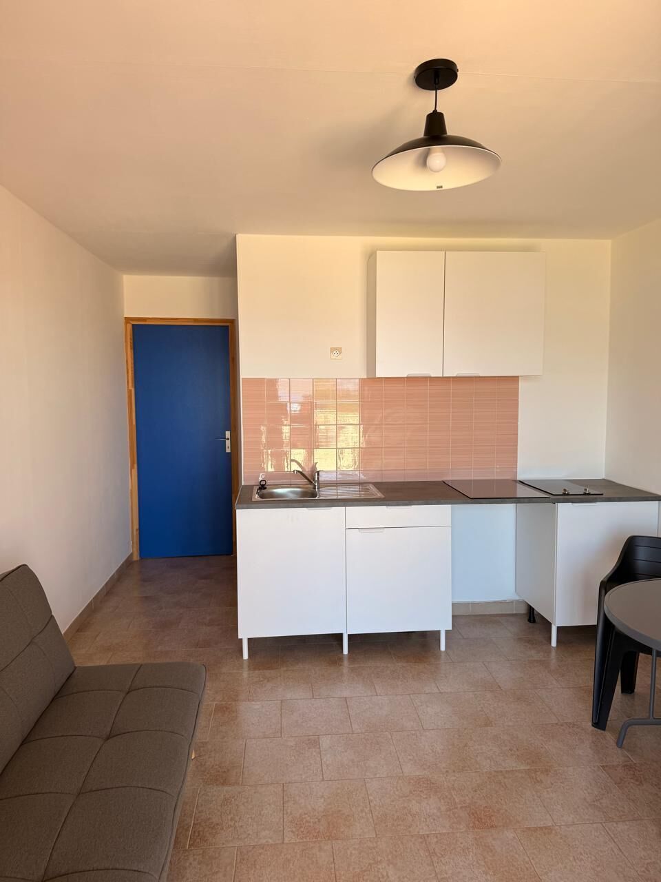 A compact kitchen with white cabinets, a countertop, and a single hanging light fixture.