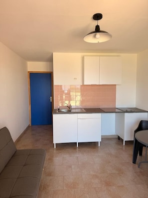 A compact kitchen with white cabinets, a countertop, and a single hanging light fixture. - Beautiful one-bedroom apartment in a house with a view of the sea, a 5-minute walk from the beach. (Calcatoggio)