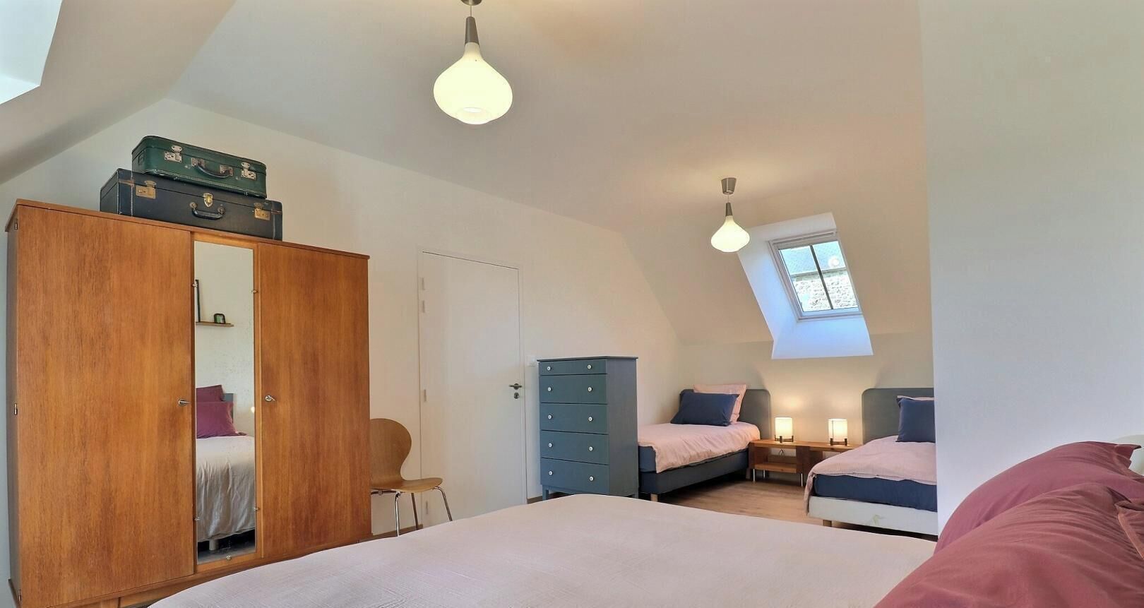 Une chambre avec un grand lit, deux petits lits, une armoire, un bureau et une fenêtre de toit.