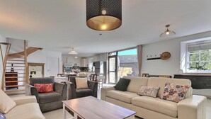 A modern living room with a sofa, chairs, a coffee table, a staircase, and a kitchen in the background. - l'Escale 1822 - QUEBRIAC (QUEBRIAC)