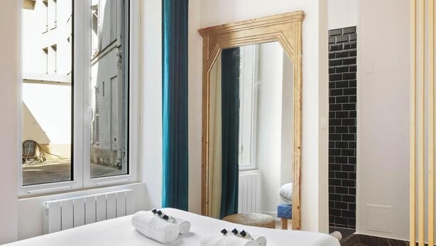 A hotel room with a bed, a large mirror, a window with curtains, and a view of buildings outside. - Suite Lumineuse en plein coeur du Marais (Paris)