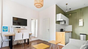 A modern living room with a TV, dining table, chairs, and a sofa. - Suite Lumineuse en plein coeur du Marais (Paris)