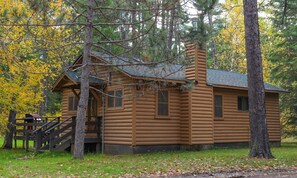 A log cabin with a porch, surrounded by trees with yellow leaves. - The Cougar Cabin at Timber Bay (Babbitt)