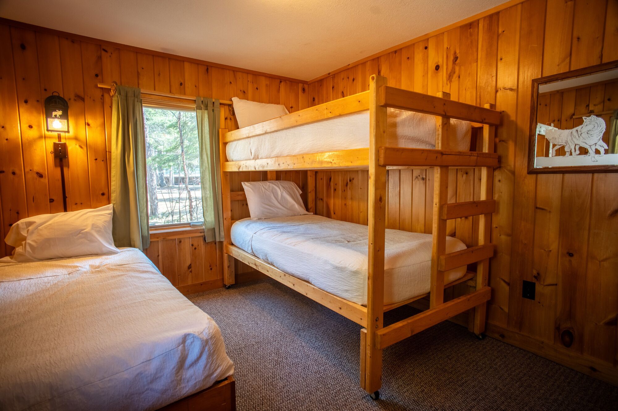 Une pièce de cabane en bois avec des lits superposés, une fenêtre avec des rideaux et un luminaire fixé au mur.