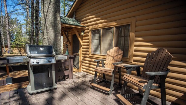 Eine Holzhütte mit Grill, Stuhl und Tisch auf der Terrasse.