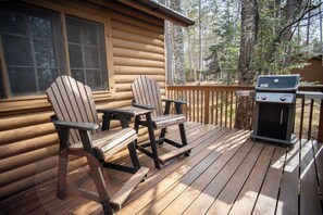 A wooden deck with Adirondack chairs, a grill, and a cabin in a forested area. - The Partridge Cabin at Timber Bay (Babbitt)