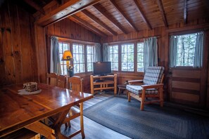 A wooden cabin interior with a dining table, chairs, a television, and a sofa. - The Fox Cabin at Timber Bay (Babbitt)