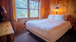 A wooden-paneled room with a bed, a nightstand, a lamp, and a window with curtains. - Prime location: The Coyote Cabin (Babbitt)
