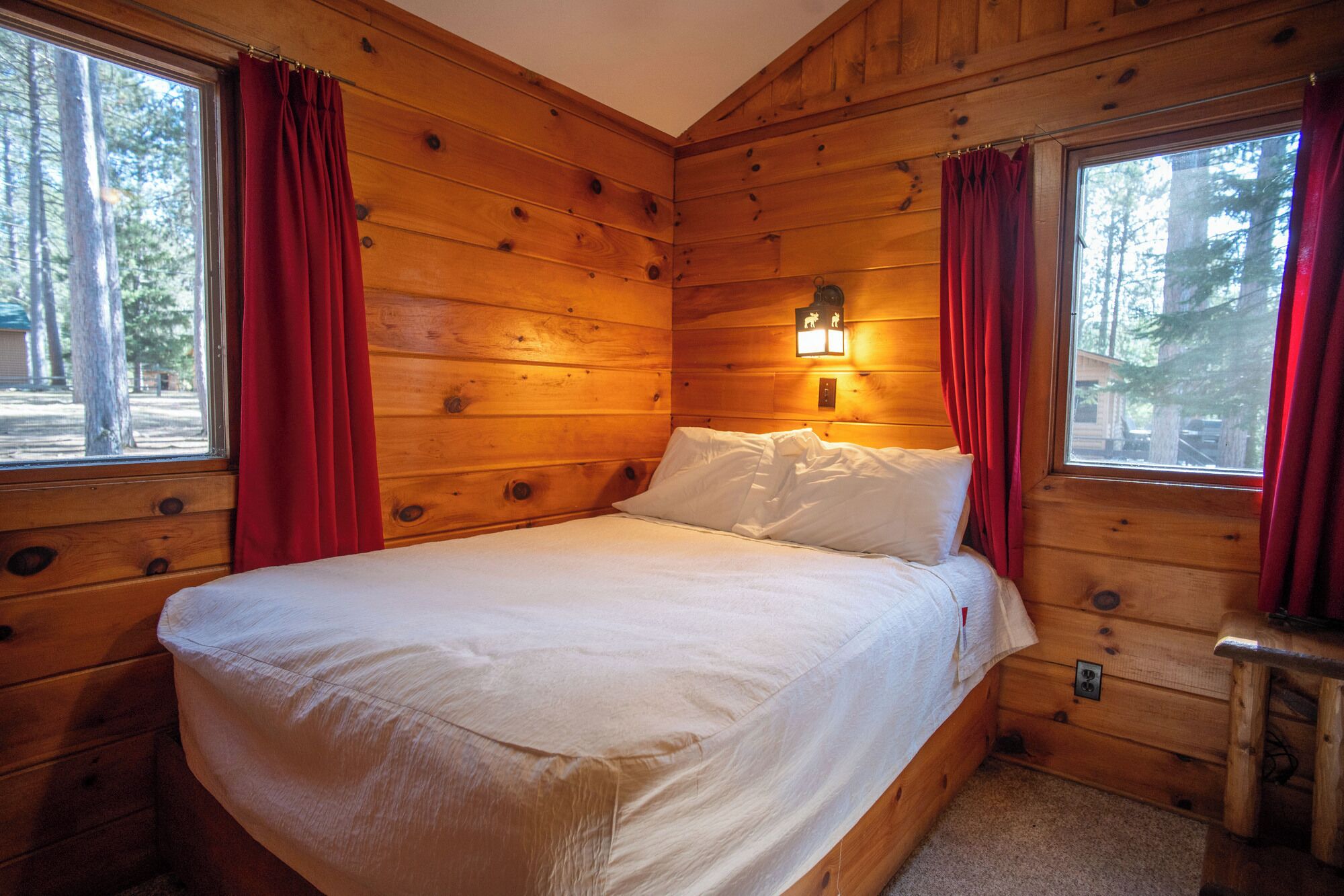 Een houten kamer met een bed, rode gordijnen en een nachtlampje.
