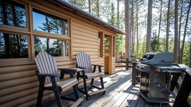A wooden cabin with a deck, two Adirondack chairs, a grill, and a table. - For our honeymooners: The Hummingbird Cabin (Babbitt)
