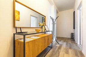 A hallway with a wooden console table, a mirror, a coat rack, and a door.